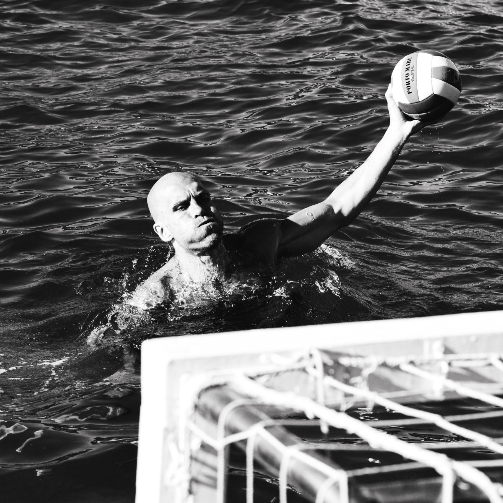 Water polo player raising the ball in open water near the goal